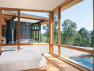 Large brown Marvin windows covering from top to bottom the walls of a bedroom overlooking a patio area and pool