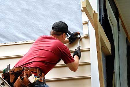 HartHaus Homes images - worker hammering in new beige siding on a home